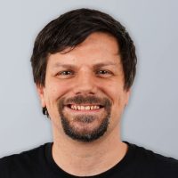 csm_Martin_Kahl_2_c716c7a55b Ein Mann mit kurzen dunklen Haaren, einem Schnurrbart und einem Spitzbart lächelt. Er trägt ein schwarzes Hemd und steht vor einem schlichten hellgrauen Hintergrund.
